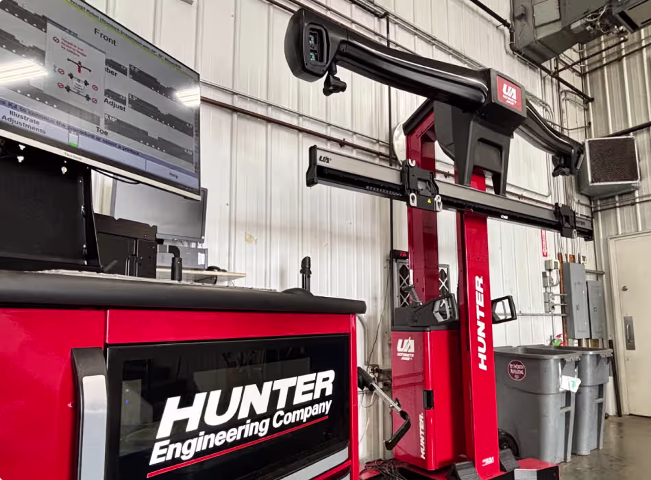 A Hunter Engineering Company wheel alignment machine stands in an automotive workshop, with a monitor displaying alignment data and various equipment visible in the background.